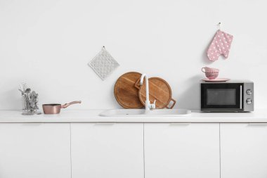 Beyaz tezgahlarda mikrodalga fırın, lavabo ve mutfak aletleri olan bir mutfak.