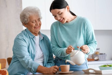 Genç bir kadın mutfakta annesi için sıcak çay dolduruyor.