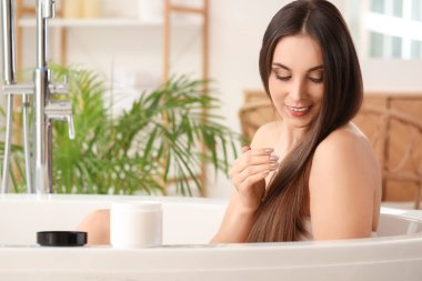 Genç esmer kadın banyoya saç ürünü sürüyor.