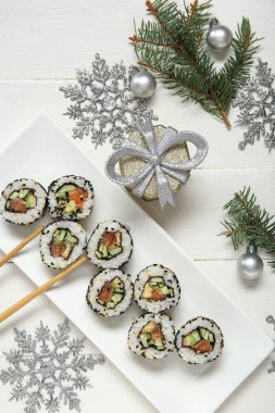 Köknar dallı lezzetli suşi ruloları, hediye kutusu ve beyaz ahşap arka planda Noel süslemeleri.