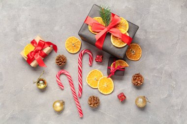 Kurumuş portakal dilimleri, baston şekerler ve gri arka planda çam kozalakları olan hediye kutuları.