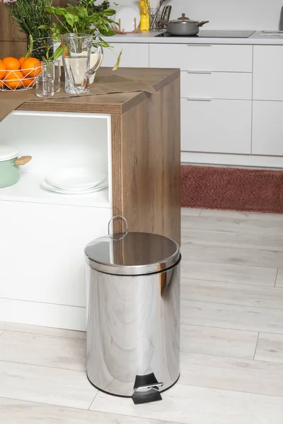 Metallic trash bin near table in interior of modern kitchen