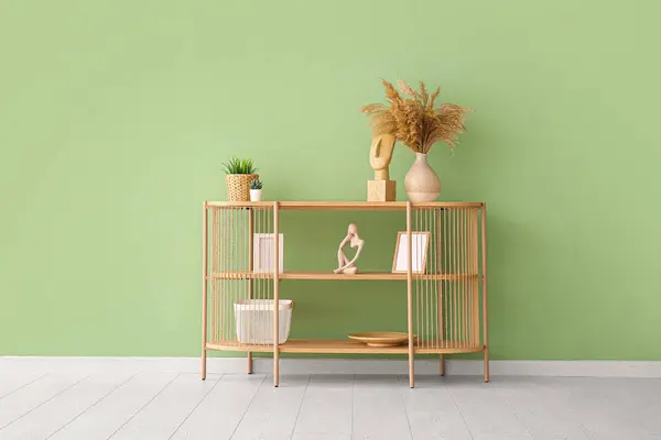 Modern shelving unit with pampas grass, houseplants and decor near green wall in room