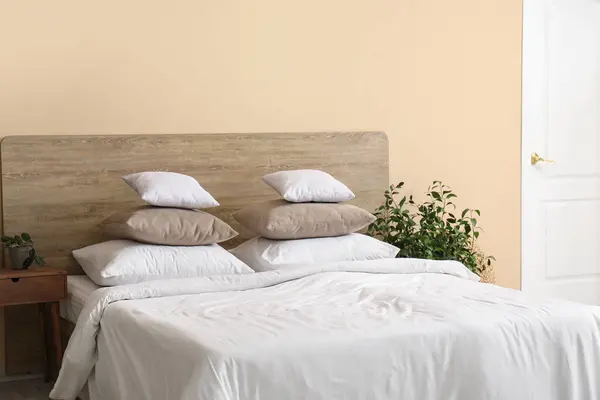 Comfortable bed with white pillows and houseplant in bedroom