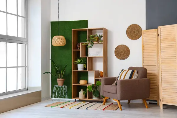 Interior of light living room with brown armchair, wicker lamp and shelving unit