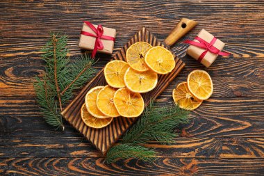 Kurumuş portakal dilimleri, köknar dalları ve tahta arka planda hediye kutuları.