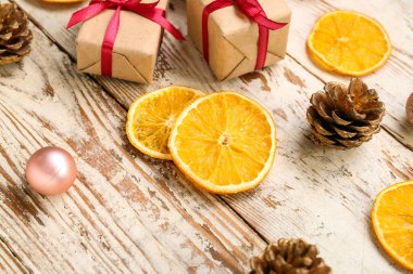 Hediye kutularıyla kurumuş portakal dilimleri, beyaz ahşap arka planda Noel topu ve çam kozalakları.