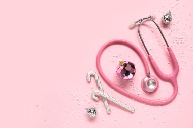 Steteskoplu kompozisyon ve pembe arka planda güzel Noel süslemeleri.