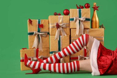 Noel çoraplı seksi kadın yeşil arka planda hediyelerin ve dekorasyonların yanında yatıyor.