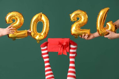 2024 model folyodan yapılmış elleri, Noel çoraplı kadın bacakları ve yeşil arka plandaki hediye kutusu.