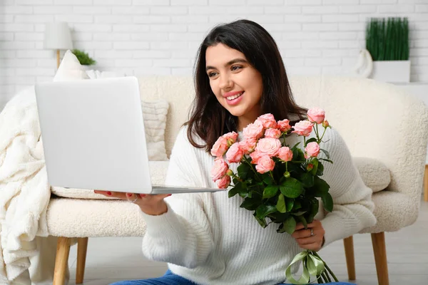Young woman with roses and laptop video chatting on online date at home