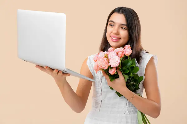 Young woman with roses and laptop video chatting on beige background. Online dating concept