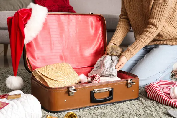 Woman packing warm clothes, passport and Christmas decor into suitcase at home