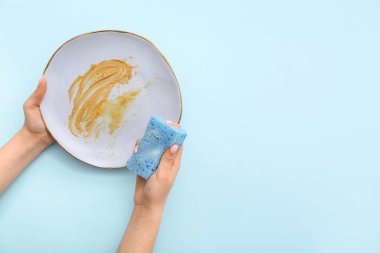 Kadın elleri kirli tabakları süngerle yıkıyor mavi arka planda