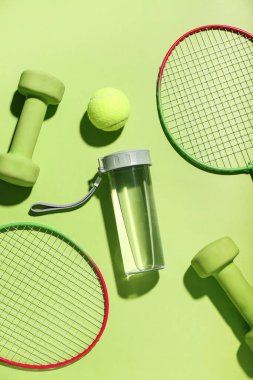 Su şişesi, dambıl, tenis raketi ve yeşil arka planda top kompozisyonu
