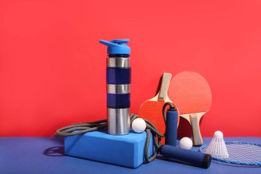 Bir şişe su ve renkli arka planda farklı spor ekipmanları