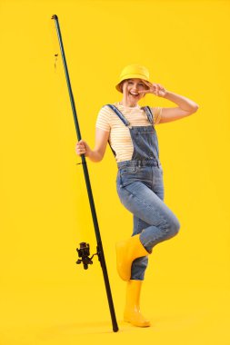 Happy young woman with fishing rod on yellow background clipart