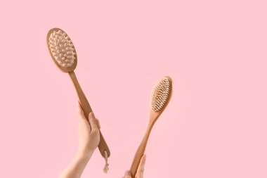 Pembe arka planda tahta masaj fırçaları tutan kadın eller.