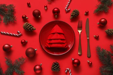 Kırmızı arka planda katlanmış peçete ve Noel süslemeleri ile şenlik masası