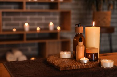 Koyu kaplıca salonundaki masada mum yakan kozmetik ürünleri, yakın plan.