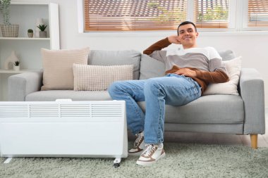 Genç adam radyatörün yanında ısınıyor.