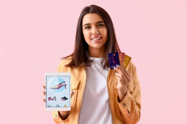Tablet bilgisayarı ve pembe arka planda kredi kartları olan genç bir kadın. İnternetten alışveriş