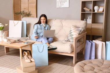 Bilgisayarlı ve kredi kartlı genç Asyalı kadın evde online alışveriş yapıyor.