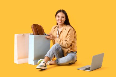 Sarı arka planda yeni çanta alışverişi yapan genç Asyalı kadın.