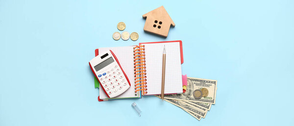 Figure of house, calculator, money and notebook on blue background
