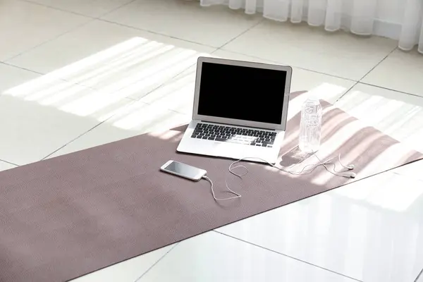 Laptop with mobile phone and earphones on fitness mat in gym
