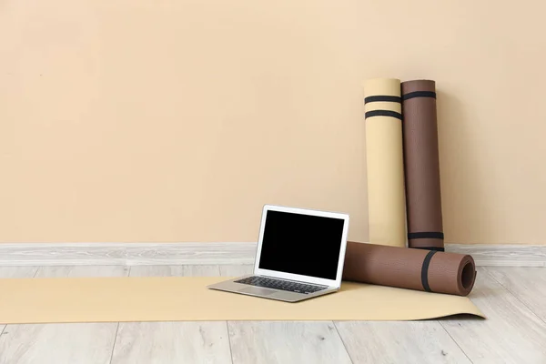 Laptop with fitness mats near beige wall in gym