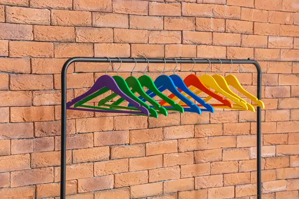 Rack with colorful hangers near brick wall