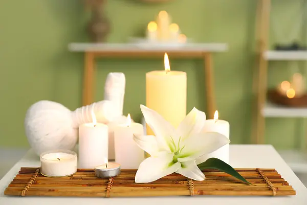 Burning candles with flower and herbal bags on table in spa salon, closeup