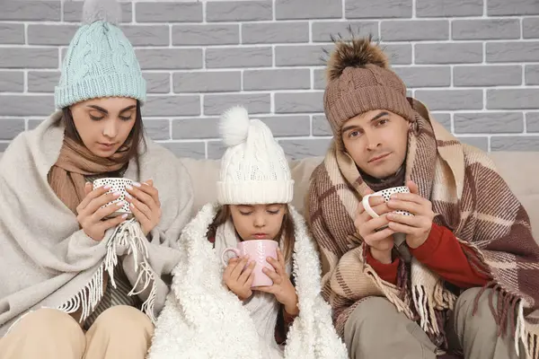 Frozen family in warm clothes drinking tea at home with lack of heating