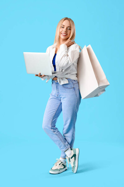 Молодая женщина с ноутбуком и сумки для покупок на синем фоне