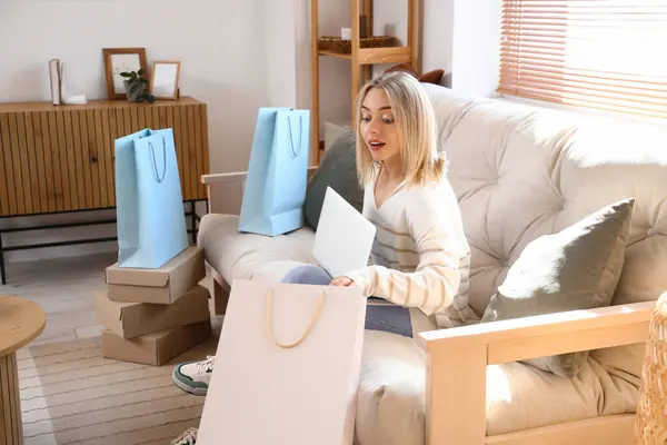 Young woman with laptop and bags shopping online at home