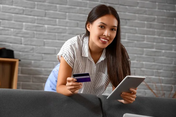 Young Asian woman with credit card and tablet computer shopping online at home