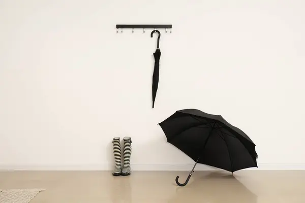Rubber boots and umbrella hanging on light wall