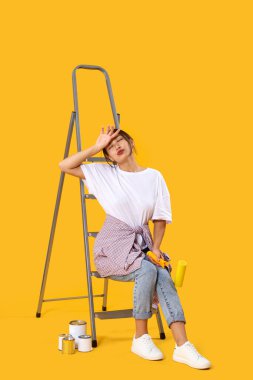 Sarı arka planda oturan yorgun Asyalı genç kadın.