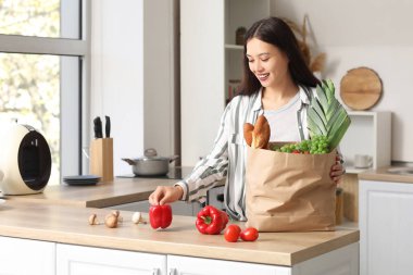 Genç Asyalı kadın mutfaktaki marketten taze ürünleri indiriyor.