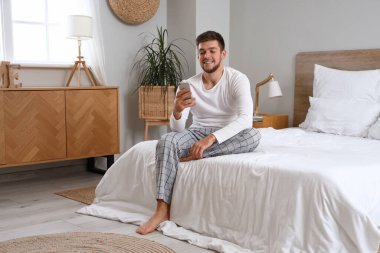 Yatak odasında cep telefonu kullanan genç sakallı adam.