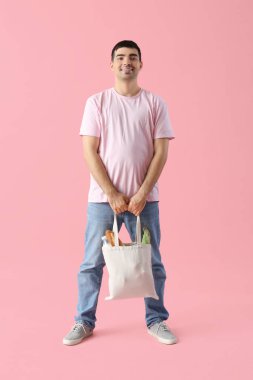 Pembe arka planda market çantalı genç adam.