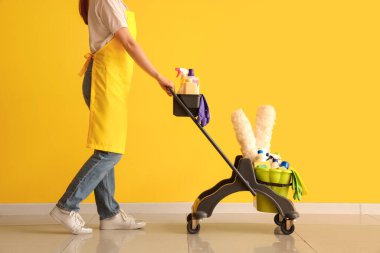 Sarı duvarın yakınındaki tramvayla temizlik malzemesi taşıyan kadın hademe.