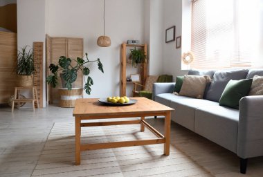 Oturma odasının iç tarafındaki ahşap sehpada limonlu rahat gri kanepe ve tabak.