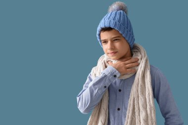 Mavi arka planda boğazı ağrıyan şapkalı hasta çocuk.