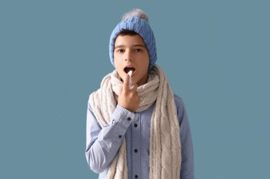 Şapkalı hasta çocuk mavi arka planda boğaz ağrısı için sprey kullanıyor.