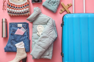 Kalın elbiseli bavul, termos ve pembe arka planda pasaport. Kış tatili kavramı