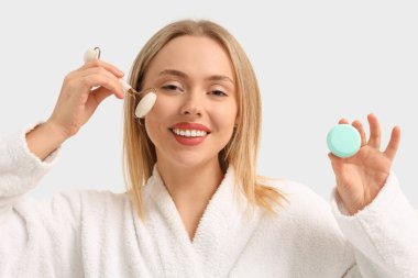 Beyaz arka planda yüz masajı ve kremi olan genç bir kadın.