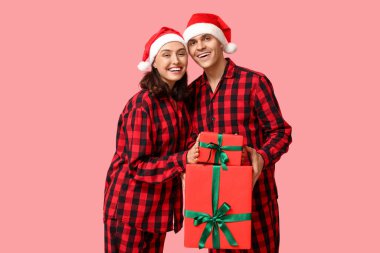 Mutlu genç çift Noel pijamalarıyla ve pembe arka planda hediyelerle