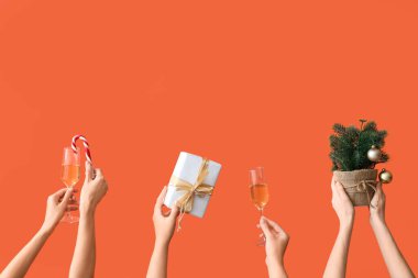 Şampanya kadehli kadın elleri ve turuncu arka planda hediyeler.
